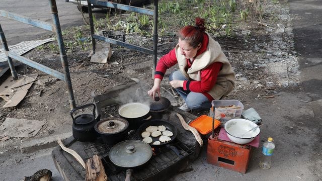 Eine Anwohnerin in Mariupol kocht am Straßenrand Essen.