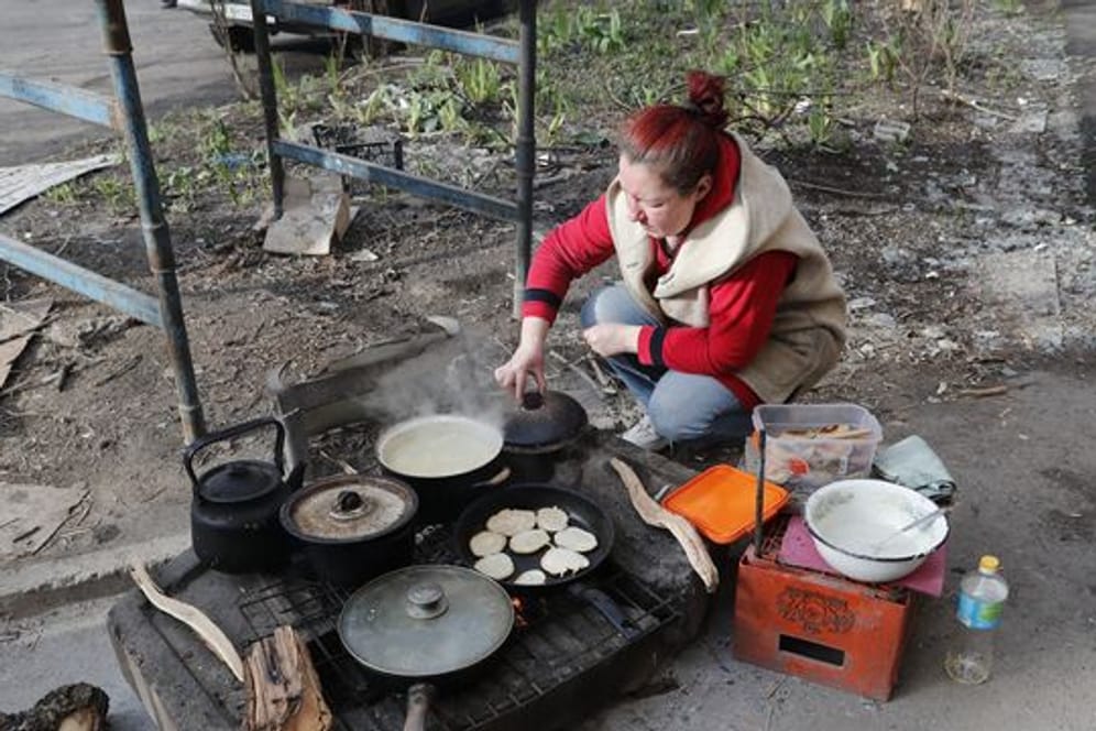 Eine Frau in Mariupol kocht am Straßenrand Essen.