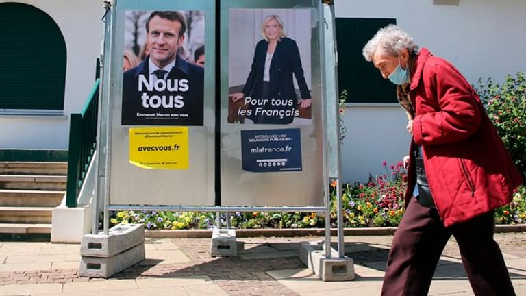 Eine Frau geht im Südwesten Frankreichs an Wahlkampfplakaten der französischen Präsidentschaftskandidaten Macron und Le Pen vorbei.