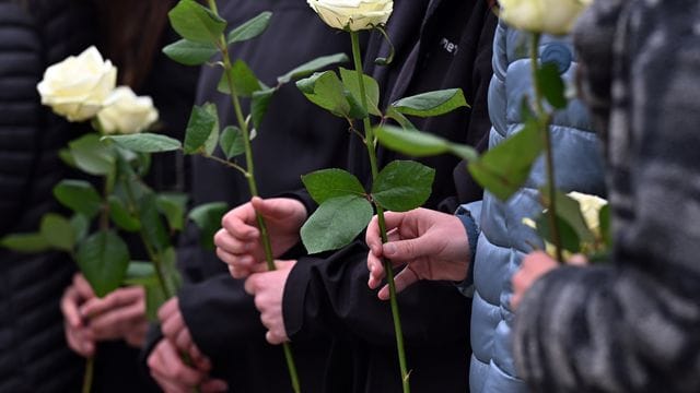 Schülerinnen und Schüler gedenken mit weißen Rosen der Opfer.