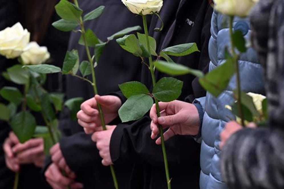 Schülerinnen und Schüler gedenken mit weißen Rosen der Opfer.