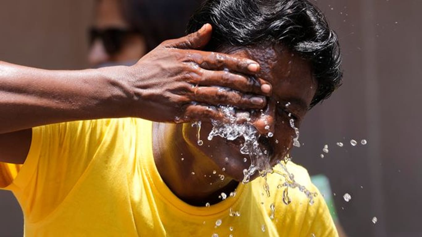 Ein Mann spritzt sich an einem extrem heißen Tag auf einem Marktplatz in Mumbai Wasser ins Gesicht.