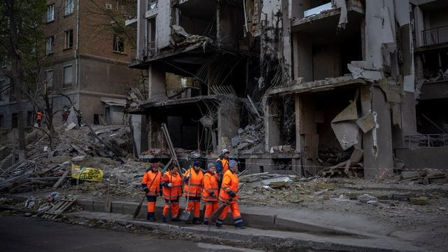 Ein Aufräumtrupp vor einem durch Raketenbeschuss zerstörten Gebäude in Kiew.