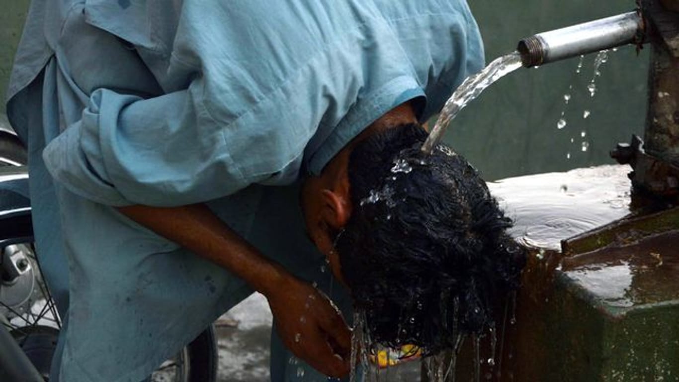 Ein junger Mann in Pakistan erfrischt seinen Kopf unter einem Wasserhahn.