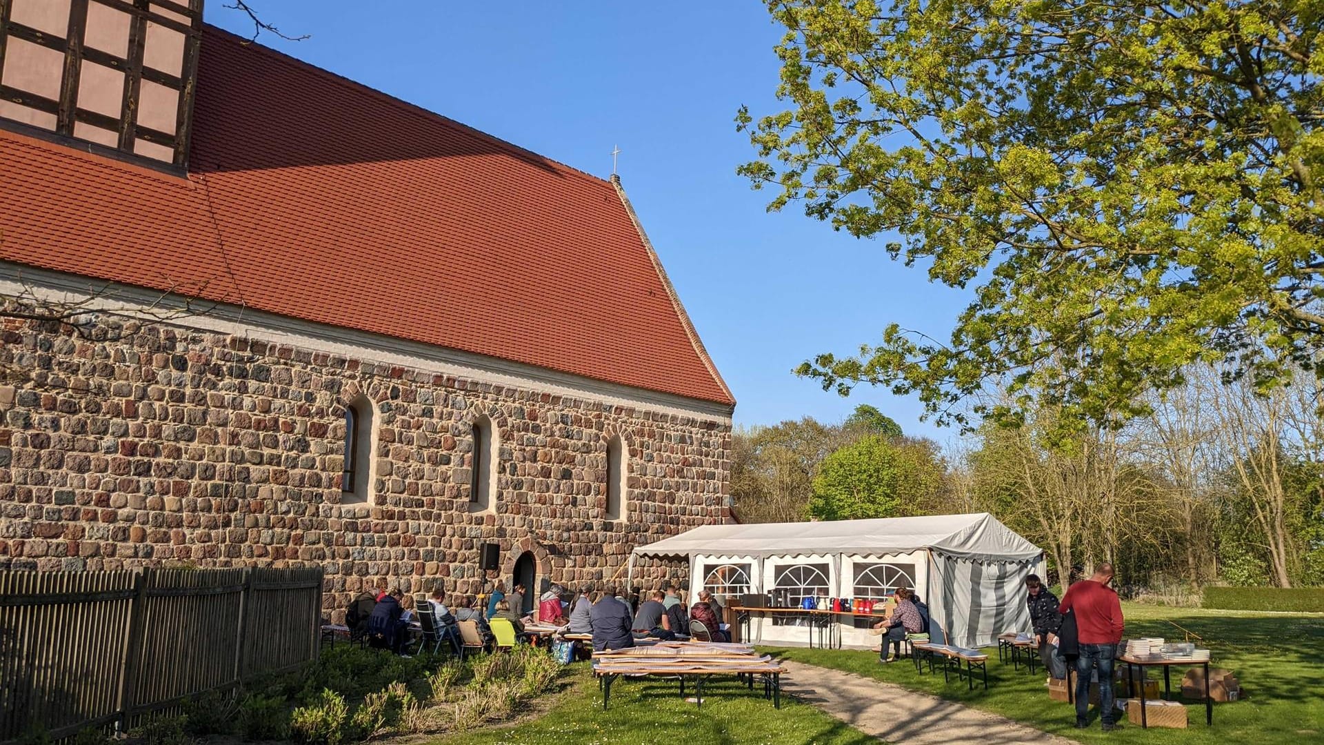 Auch vor der Kirche finden sich in Malchow einige Zuhörer ein. Bei bestem Sonnenschein wird Tee und Kaffee gereicht.