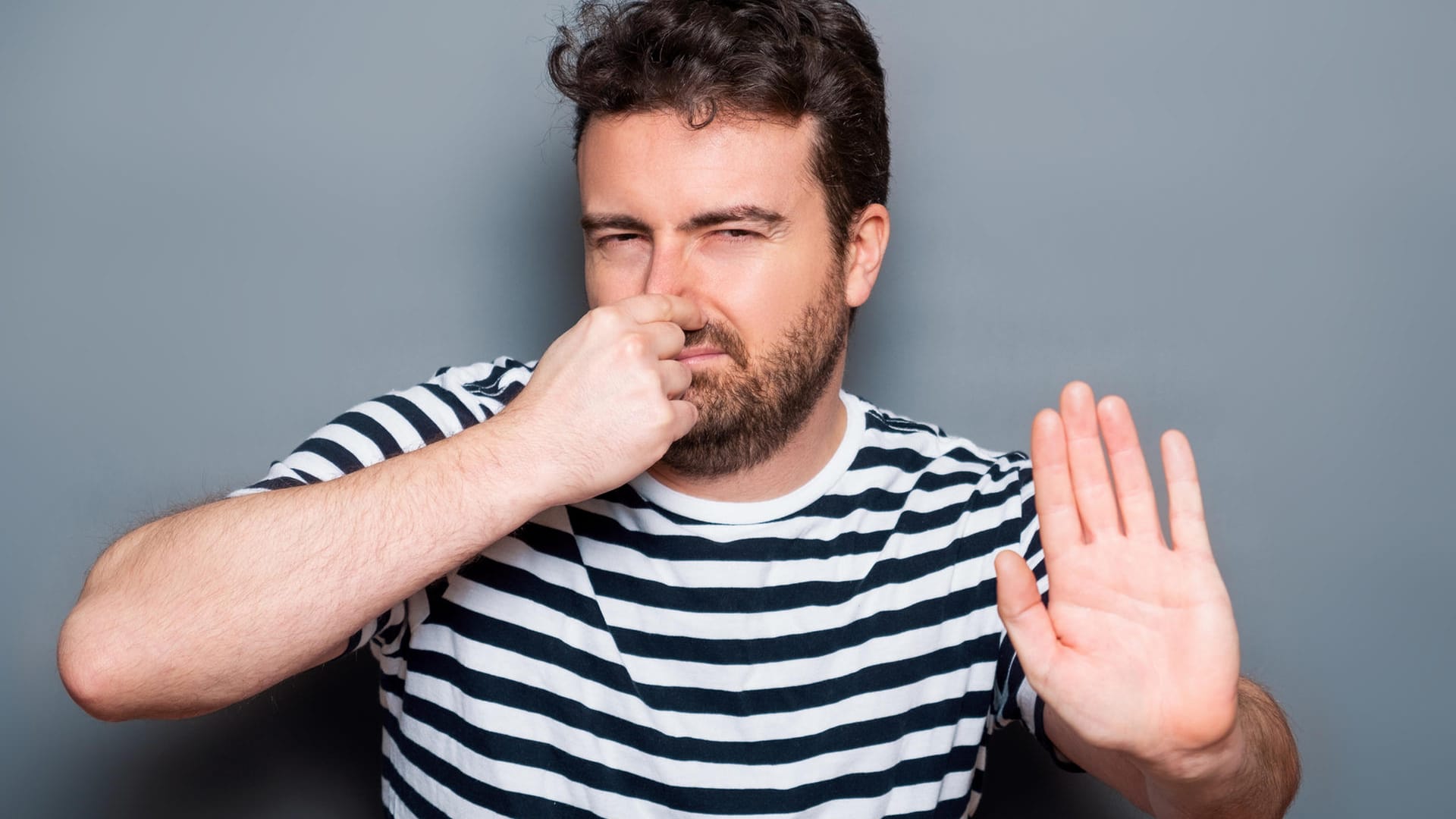 Junge Mann hält sich die Nase zu und macht mit der Hand eine ablehnende Geste