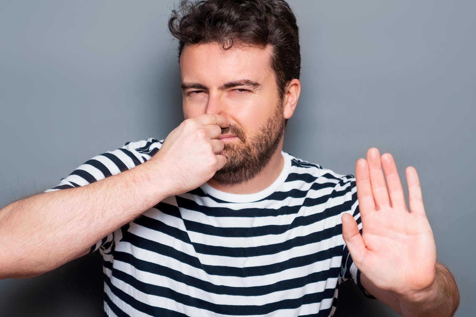 Junge Mann hält sich die Nase zu und macht mit der Hand eine ablehnende Geste