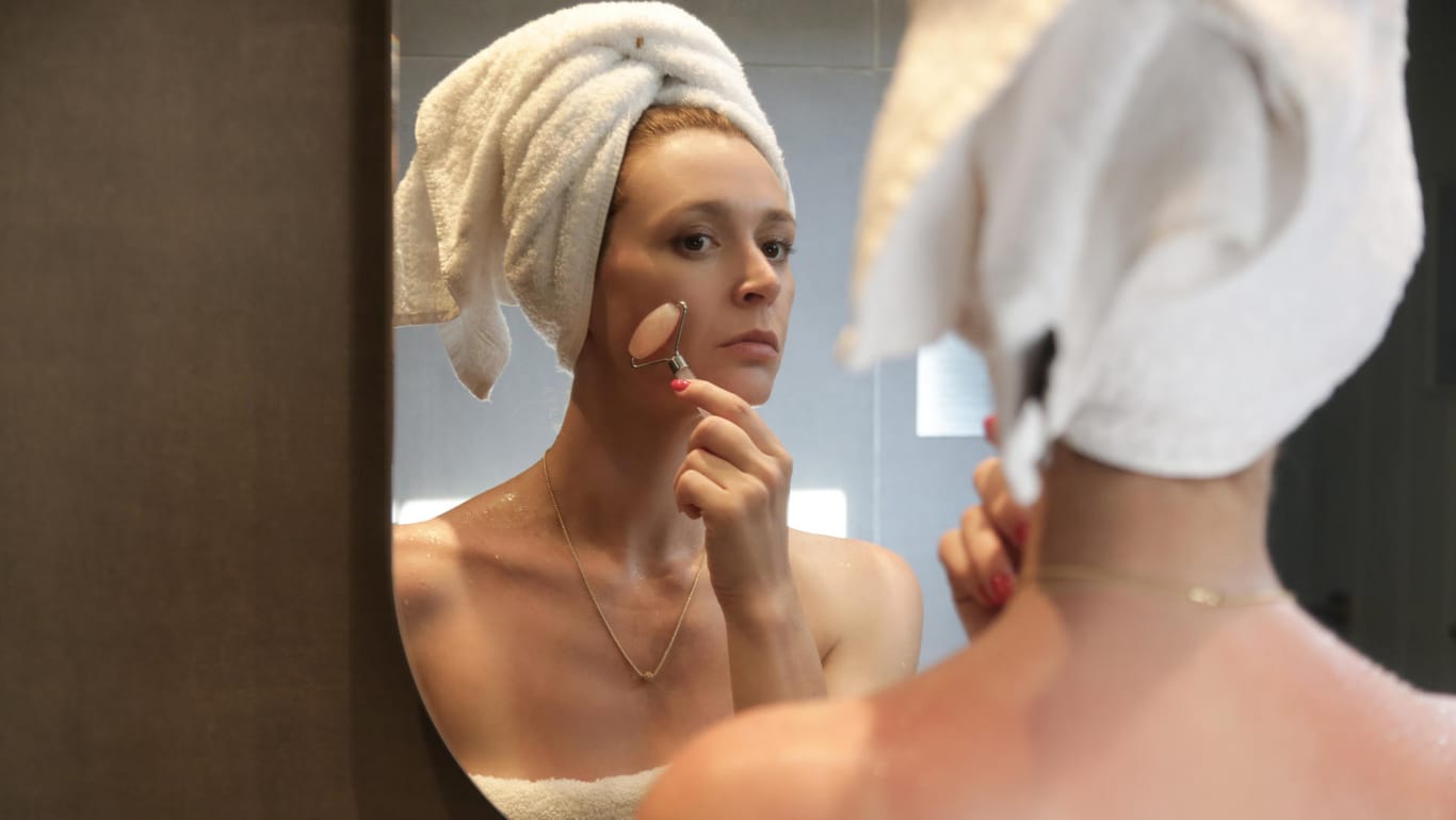 Frau vor Spiegel benutzt Gesichtsroller: Gesichtsmassagen mit Edelstein-Rollern regen die Durchblutung an und sorgen für einen frischen Teint.