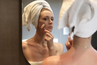 Frau vor Spiegel benutzt Gesichtsroller: Gesichtsmassagen mit Edelstein-Rollern regen die Durchblutung an und sorgen für einen frischen Teint.
