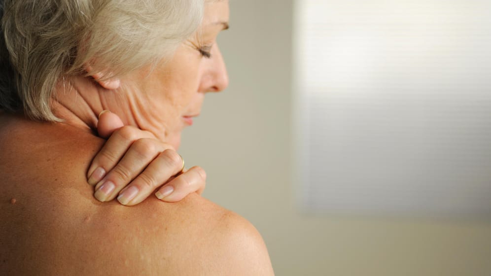 Ältere Frau fasst sich an die Schulter. Verkalkungen im Bereich der Rotatorenmanschette können starke Schmerzen verursachen und zu Versteifungen führen.