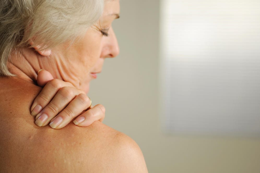 Ältere Frau fasst sich an die Schulter. Verkalkungen im Bereich der Rotatorenmanschette können starke Schmerzen verursachen und zu Versteifungen führen.