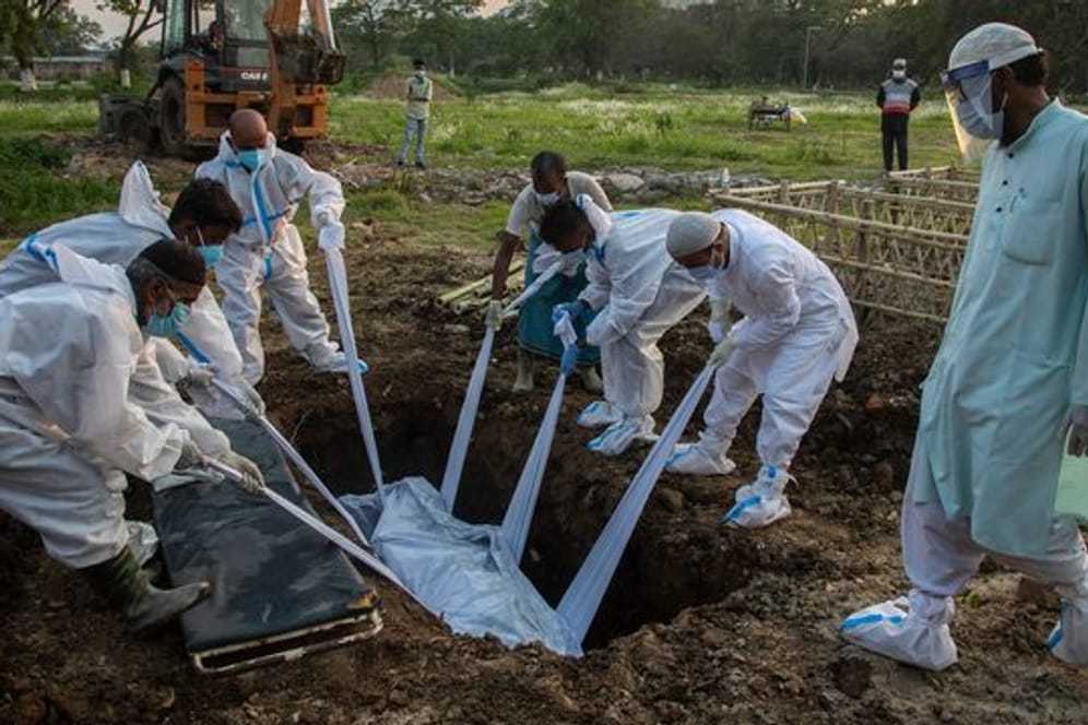 Angehörige und städtische Mitarbeiter in Schutzanzügen begraben im indischen Gauhati einen Menschen, der an Covid-19 gestorben ist.