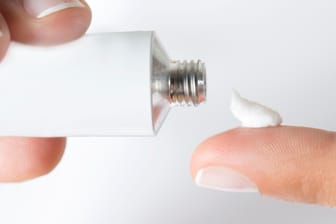 Fingerspitze mit weißer Creme neben einer Tube