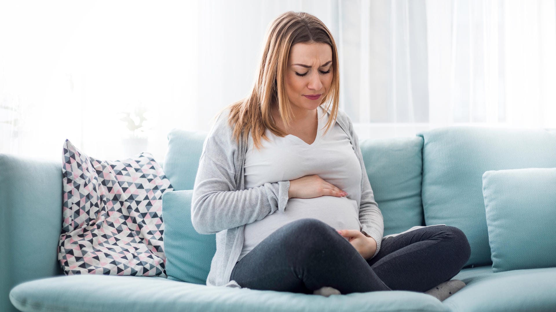 Schwangere auf dem Sofa hält sich den Bauch