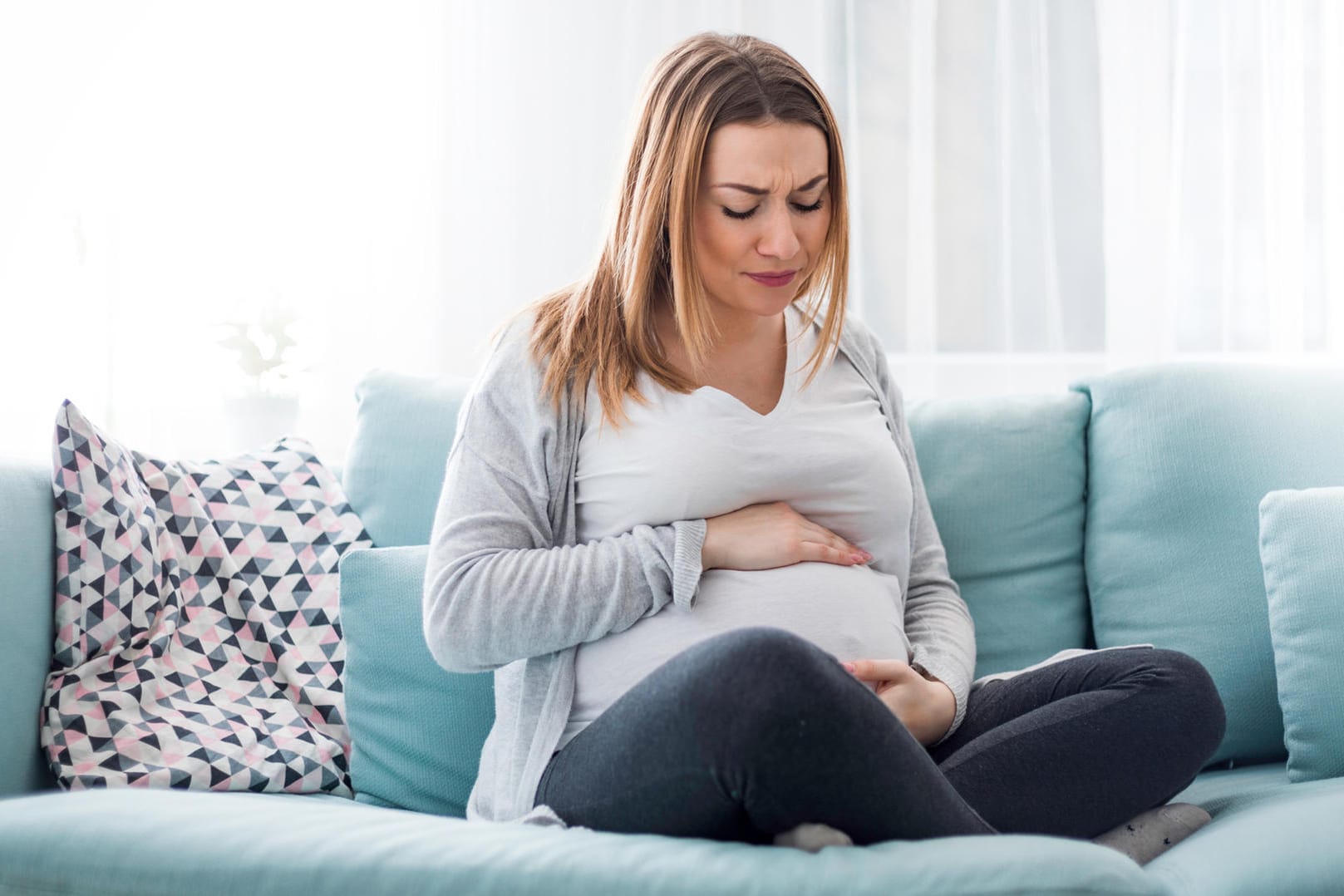 Schwangere auf dem Sofa hält sich den Bauch