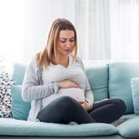 Schwangere auf dem Sofa hält sich den Bauch
