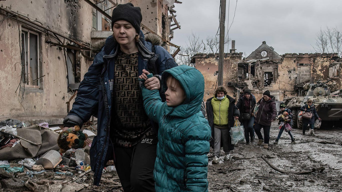 Eine Mutter mit Kind läuft durch eine zerstörte Siedlung in Mariupol: Die Stadt wird aktuell von der russischen Armee belagert.