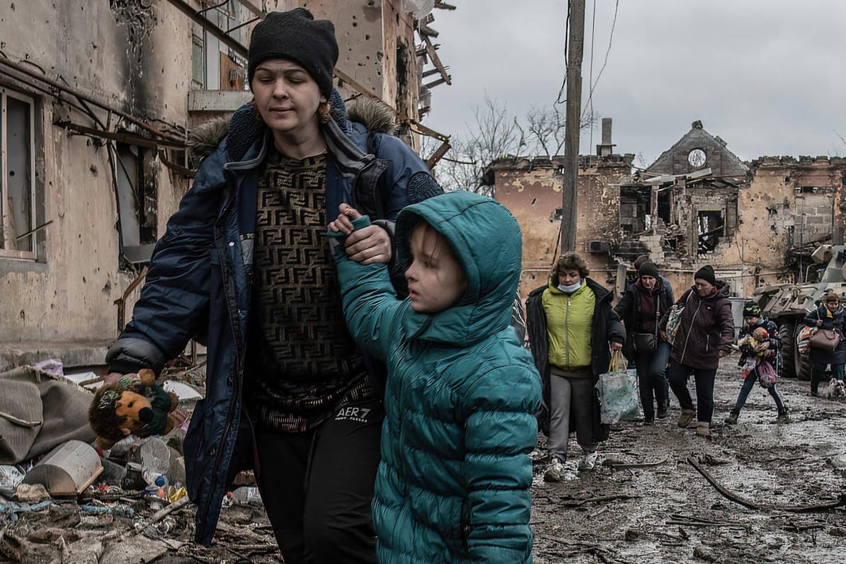 Eine Mutter mit Kind läuft durch eine zerstörte Siedlung in Mariupol: Die Stadt wird aktuell von der russischen Armee belagert.