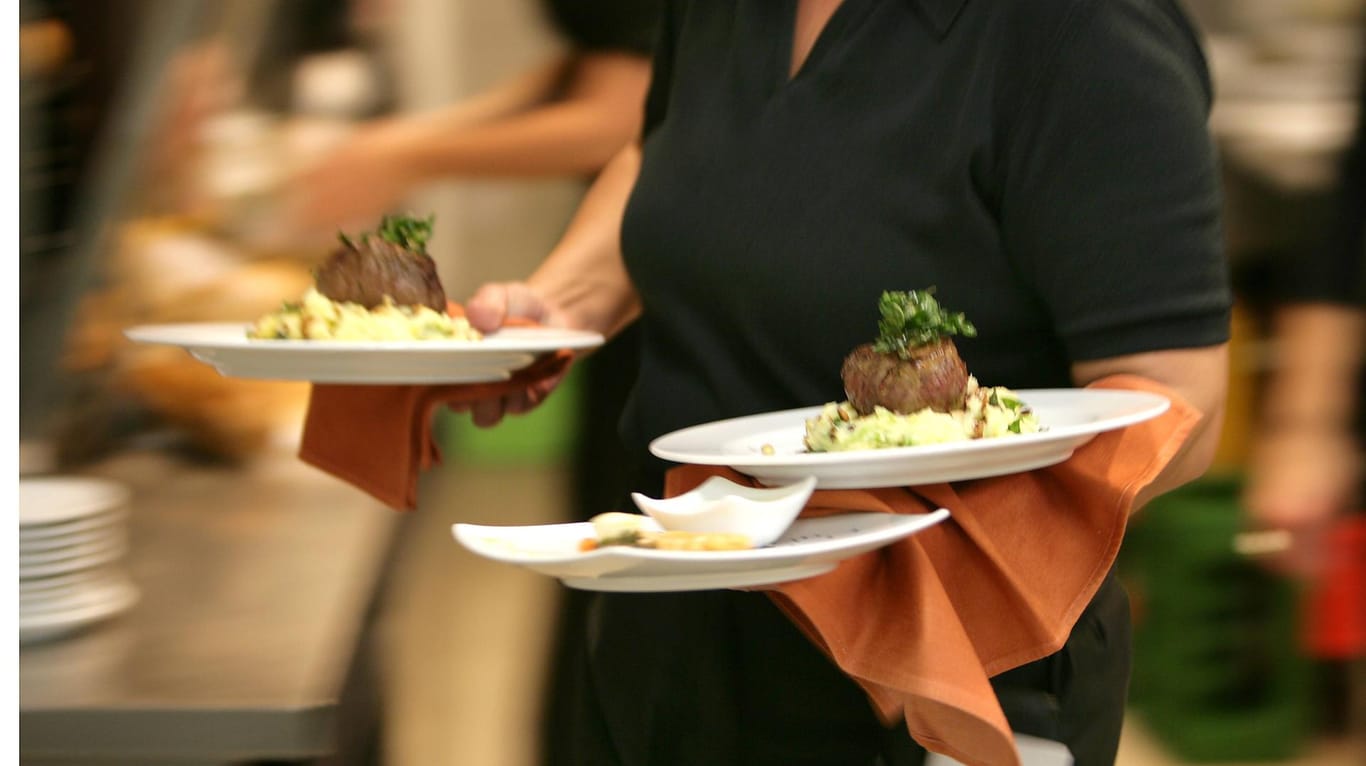 Ein Kellner bringt Teller mit Speisen (Symbolbild): Um seine Karte nicht ändern zu müssen, hat ein Gastronom einen anderen Weg gewählt, um Mehrkosten auszugleichen.