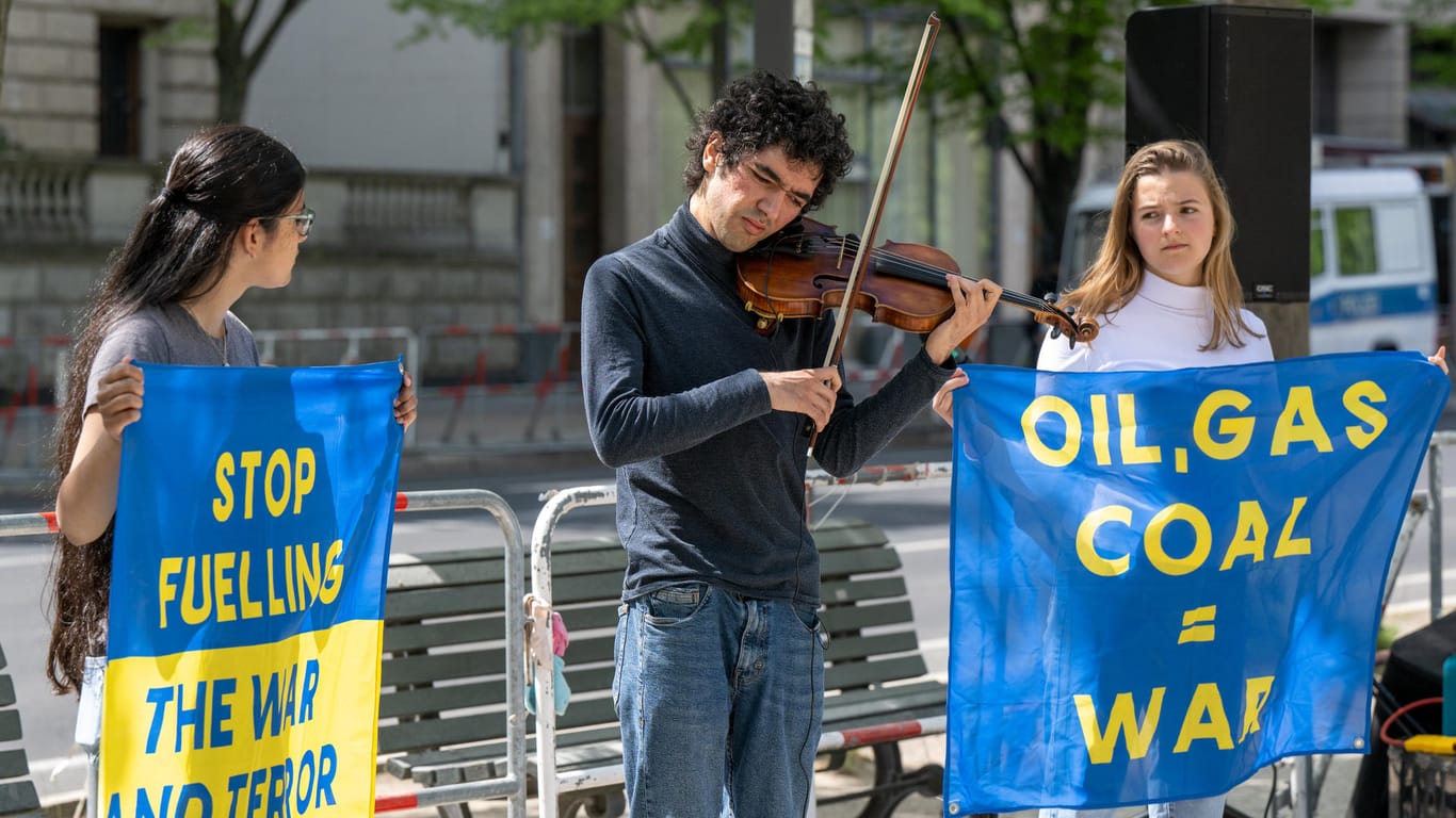 Arshak Makichyan spielt vor der russischen Botschaft auf seiner Geige, neben ihm zwei junge Umwelt-Aktivistinnen mit Transparenten.
