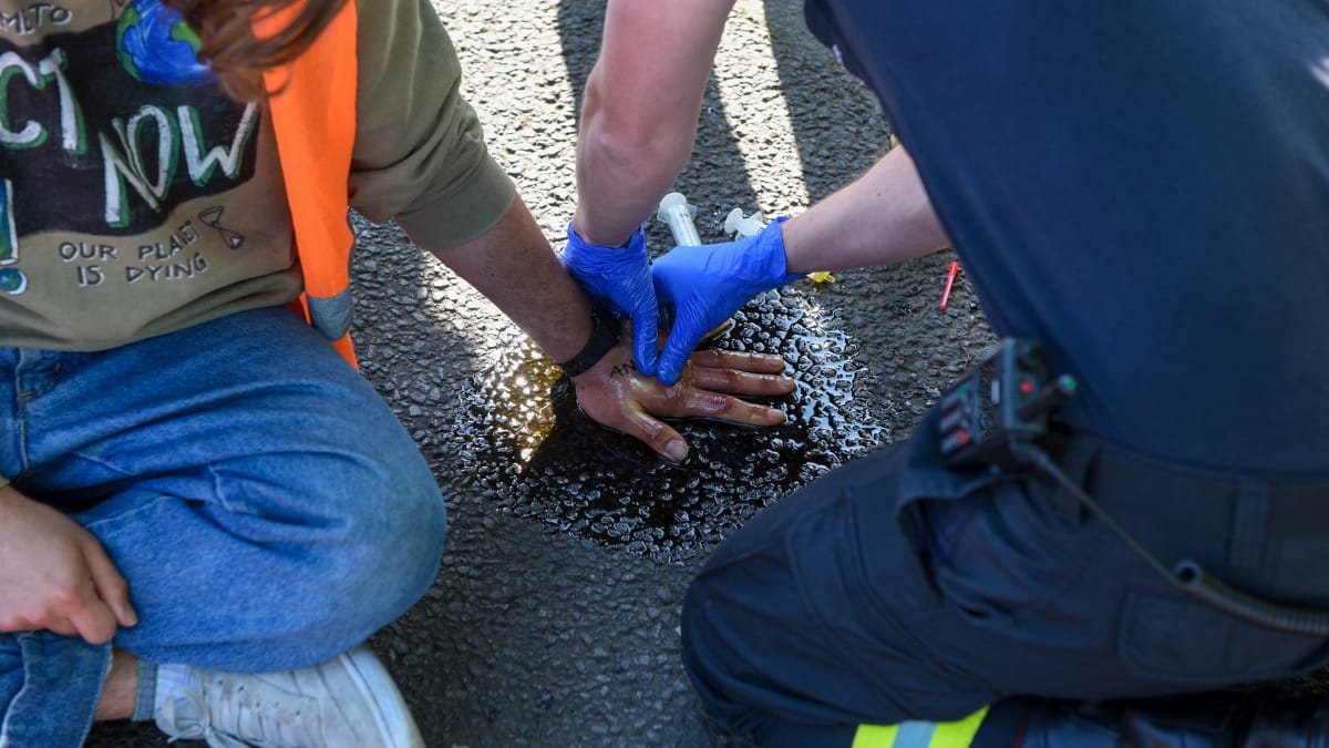 Rettungskräfte lösen die Hand eines Aktivisten vom Asphalt (Archiv): Seit Wochen blockiert die "Letzte Generation" den Vekehr.