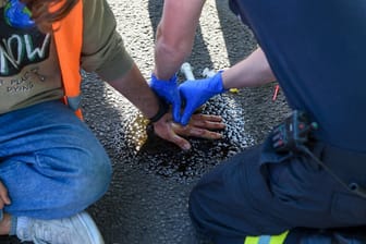 Rettungskräfte lösen die Hand eines Aktivisten vom Asphalt (Archiv): Seit Wochen blockiert die "Letzte Generation" den Vekehr.