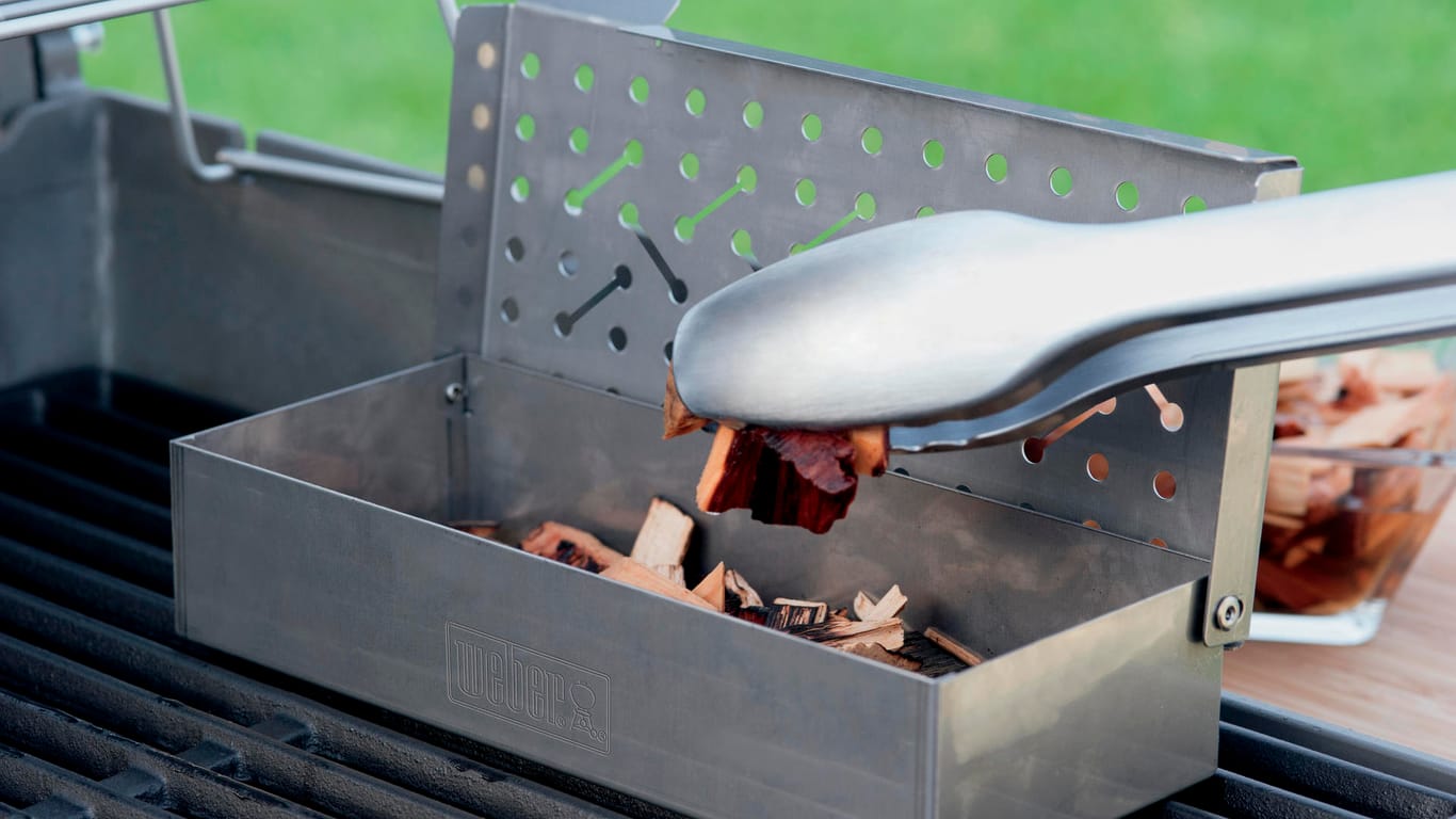 So geht's: Zum Smoken kann bei einem Gasgrill die Räucherbox mit den Räucherchips gefüllt und auf dem Grillrost neben den Speisen platziert werden. Wichtig ist nur, dass dann der Deckel geschlossen wird.