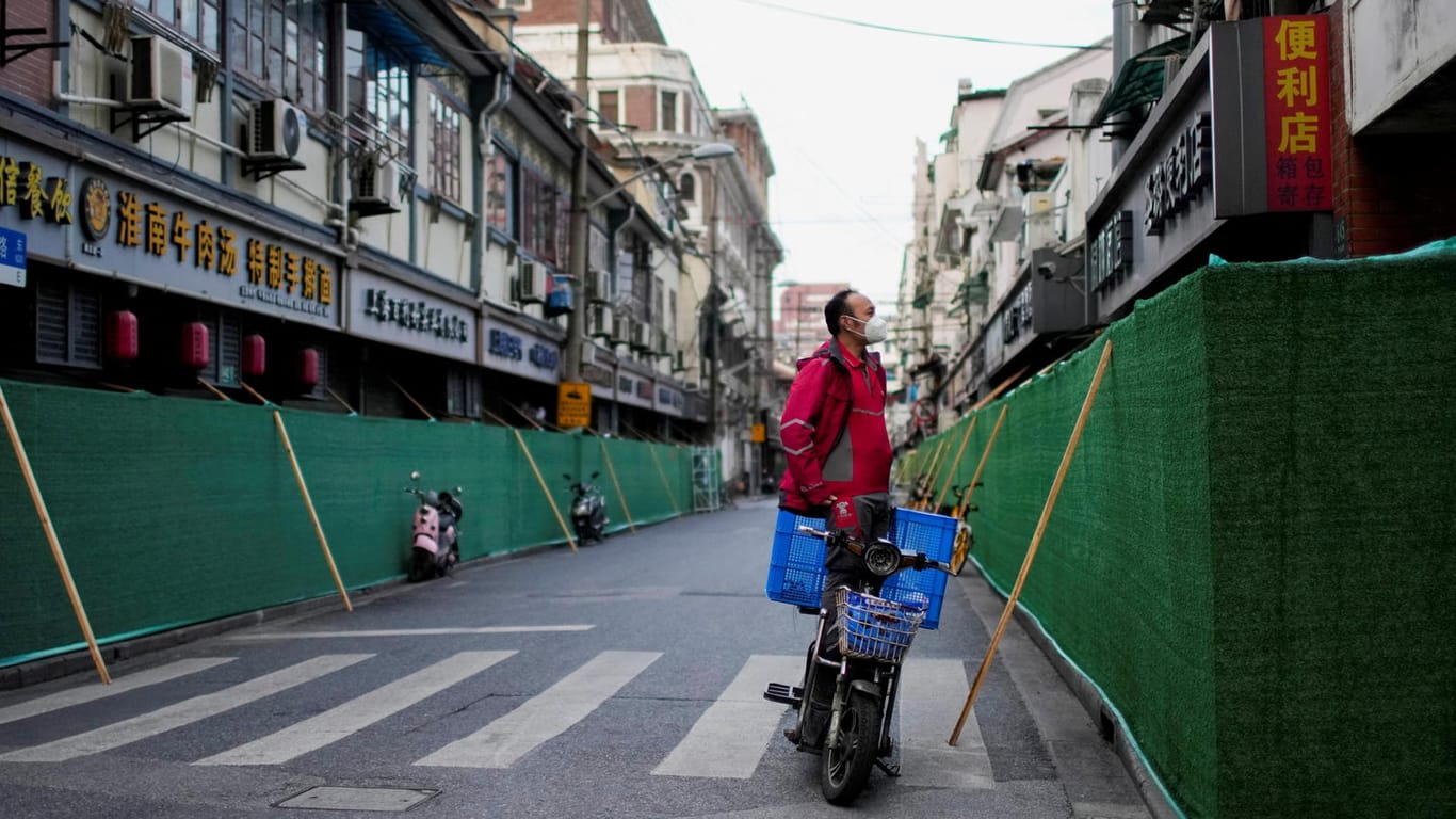 Abgeschottete Häuser in Shanghai: Ein Lieferfahrer steht vor einer Barrikade in einem Wohnviertel.
