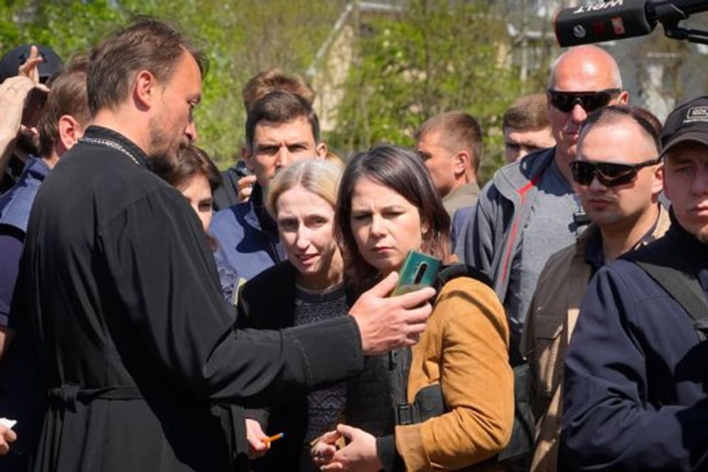 In der Nähe eines Massengrabes in Butscha spricht Annalena Baerbock mit einem örtlichen Priester, der der Außenministerin Bilder auf seinem Smartphone zeigt.