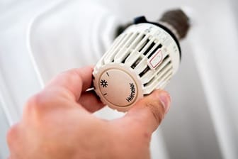 Ein Mann dreht in einer Wohnung am Thermostat einer Heizung.
