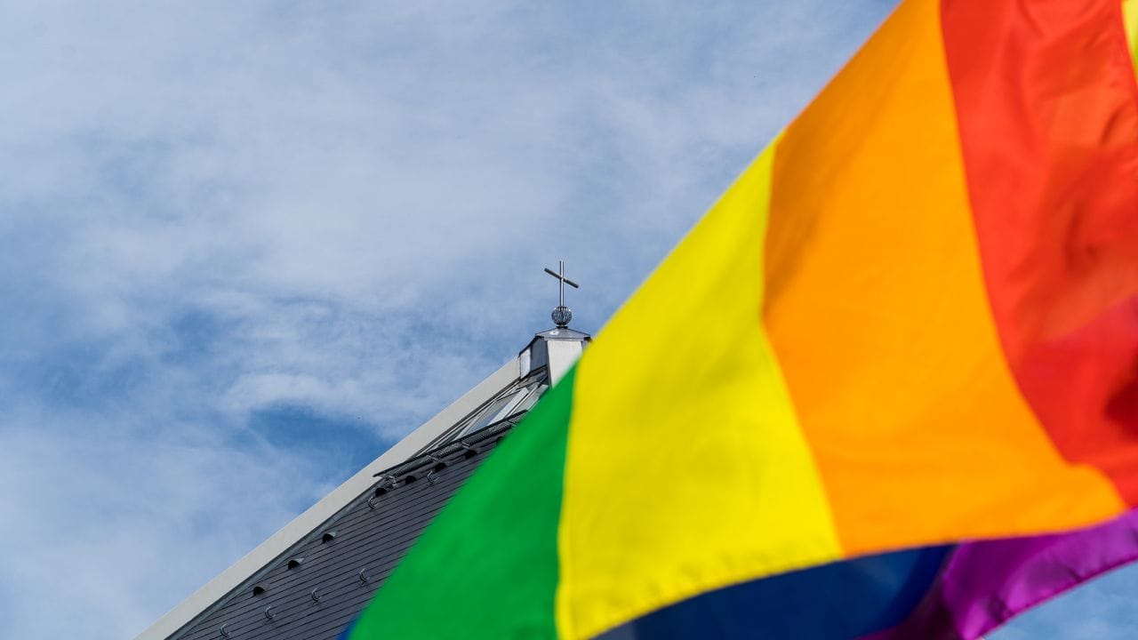 Eine Regenbogenfahne weht vor einer Kirche. Eine Regenbogenfahne weht vor einer Kirche.