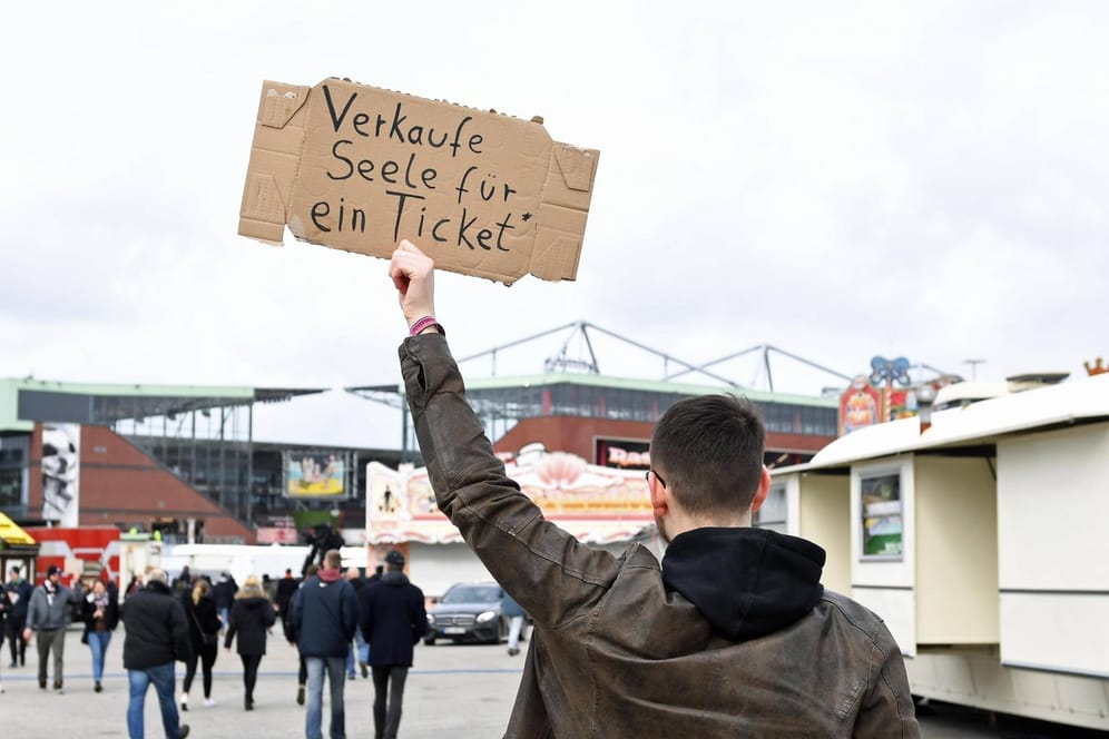 Ein Mann hält ein Schild hoch, auf dem er nach einem Ticket für ein Fußballspiel sucht (Archivbild).