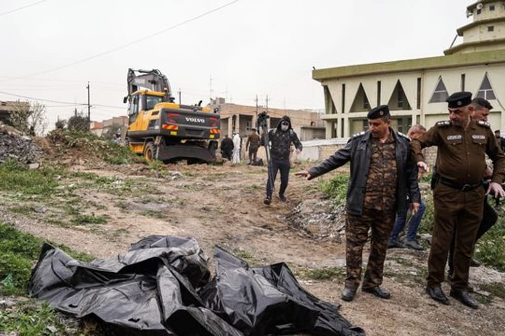 Mitglieder der Sicherheitskräfte zeigen auf einen Leichensack mit menschlichen Überresten, der in einem Massengrab im Westen von Mossul entdeckt wurde.