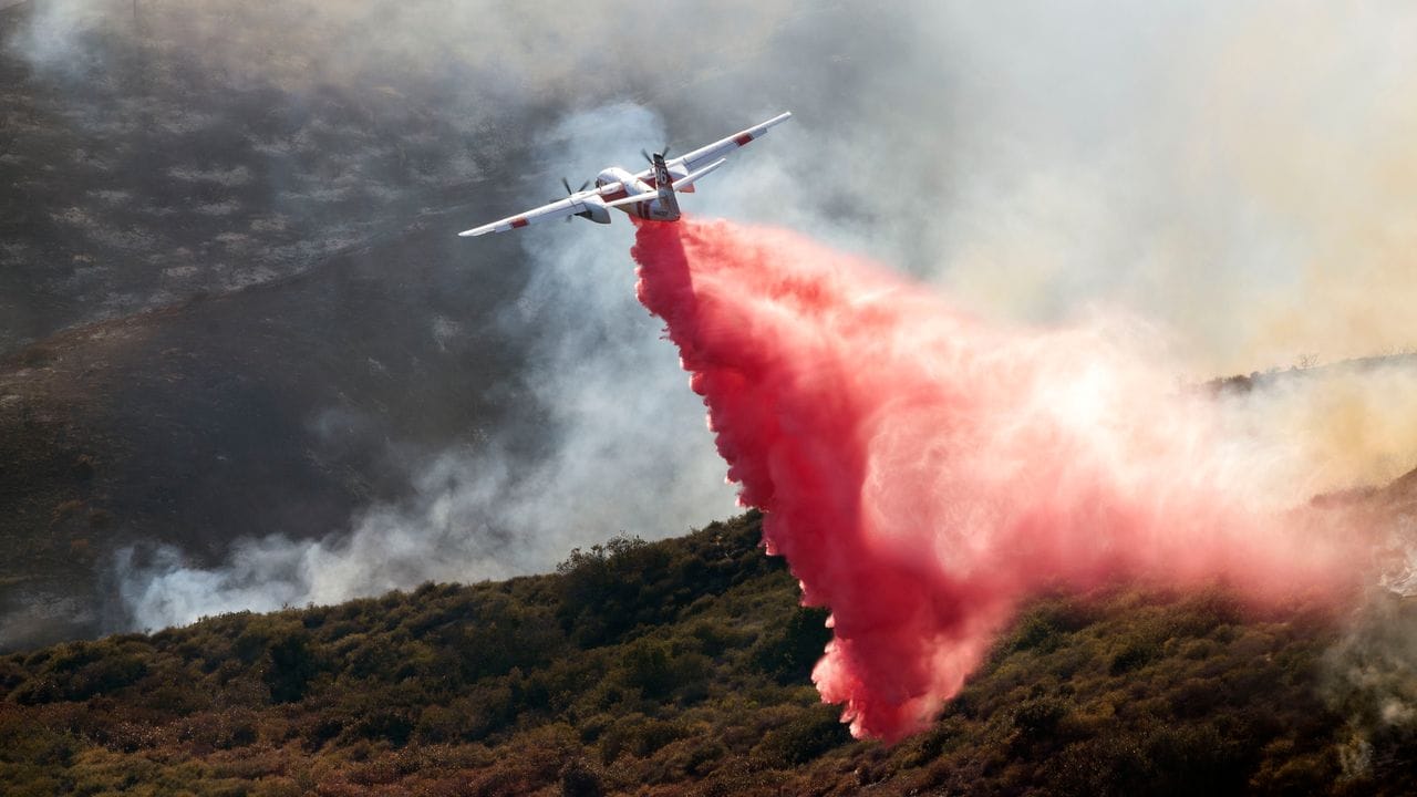 Ein Löschflugzeug wirft rotes Löschmittel auf das Küstenbuschfeuer in Laguna Niguel.