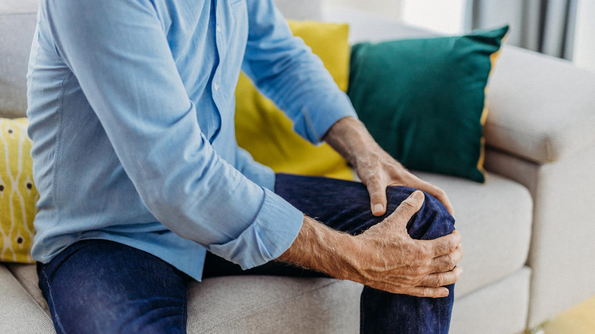 Ein sitzender Mann greift sich ans schmerzende Knie.