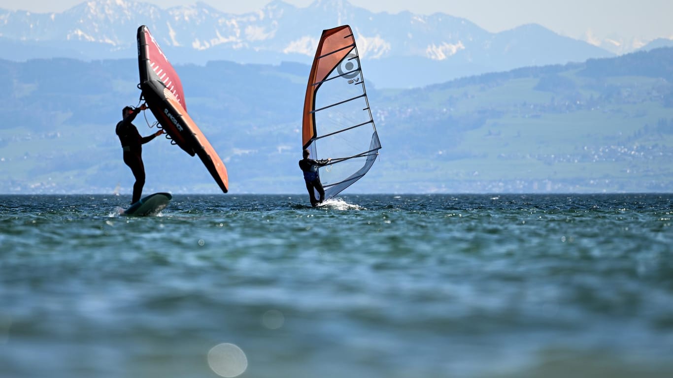 Zwei Surfer gleiten vor Immenstaad über den Bodensee, während im Hintergrund die Alpen in der Schweiz zu sehen sind.
