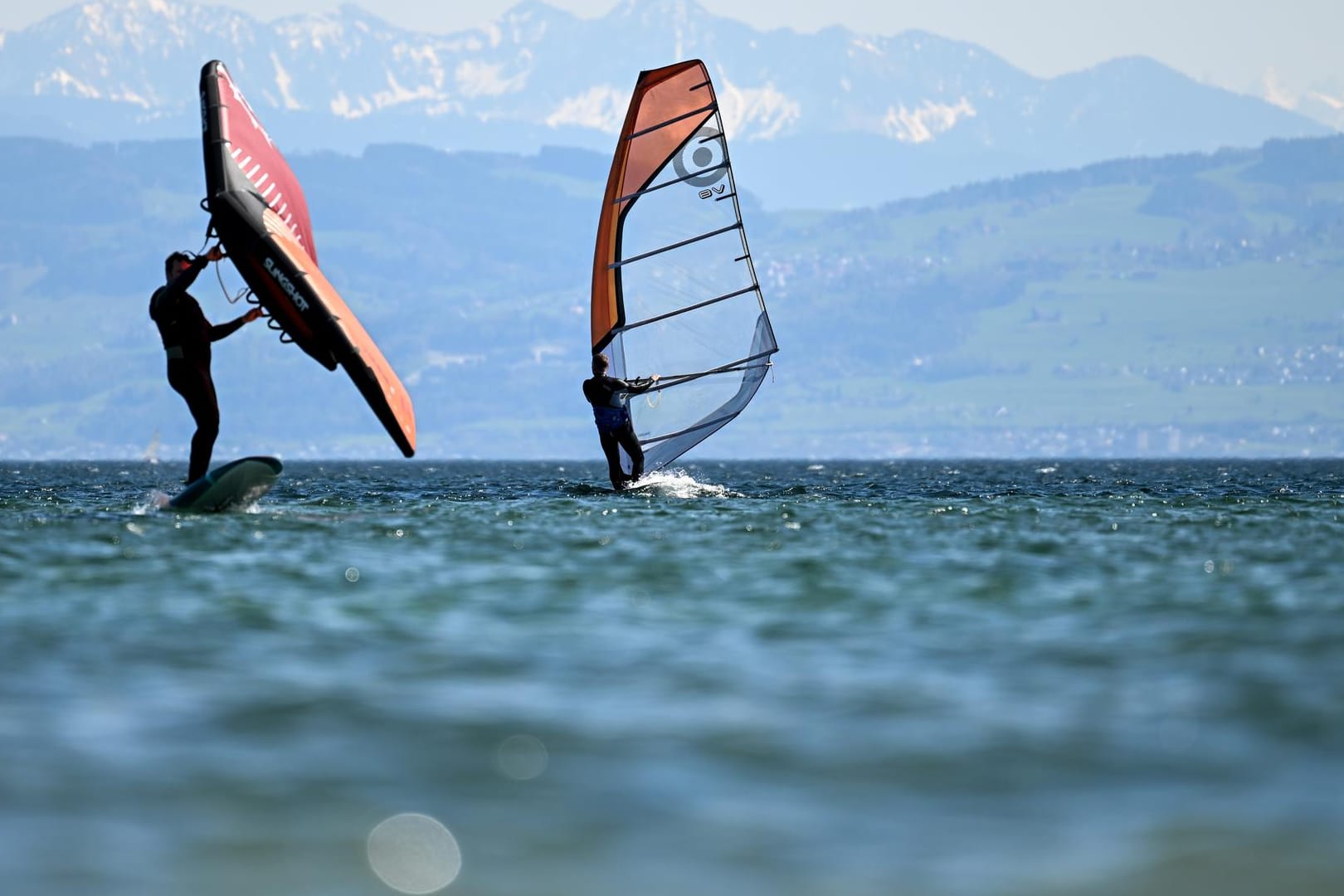 Zwei Surfer gleiten vor Immenstaad über den Bodensee, während im Hintergrund die Alpen in der Schweiz zu sehen sind.