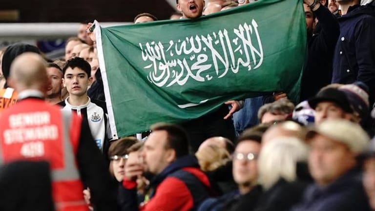 Ein Fan von Newcastle United hält die Fahne von Saudi-Arabien während eines Spiels hoch.