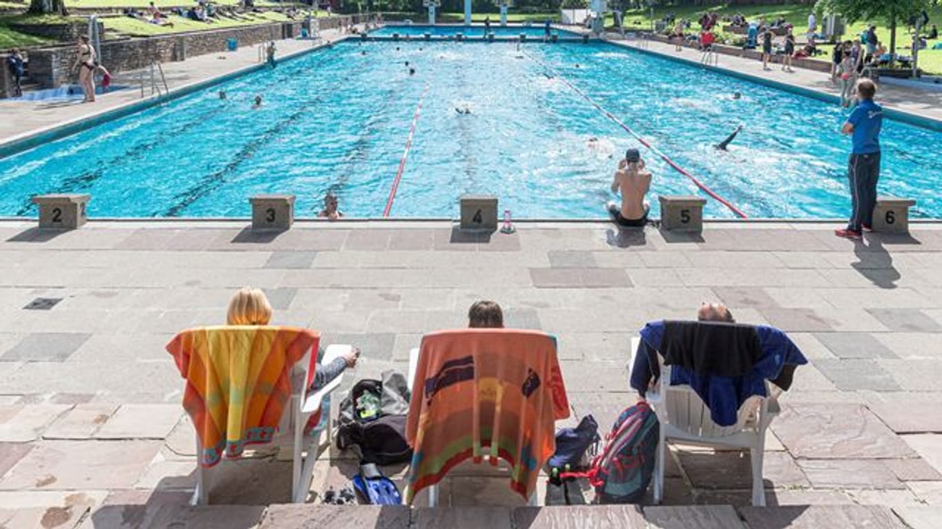 Badegäste sitzen in einem Schwimmbad in Liegestühlen (Symbolbild): Die Wassertemperatur wird in diesem Sommer in ganz München reduziert.