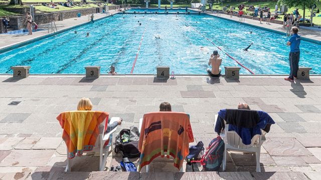 Badegäste sitzen in einem Schwimmbad in Liegestühlen (Symbolbild): Die Wassertemperatur wird in diesem Sommer in ganz München reduziert.