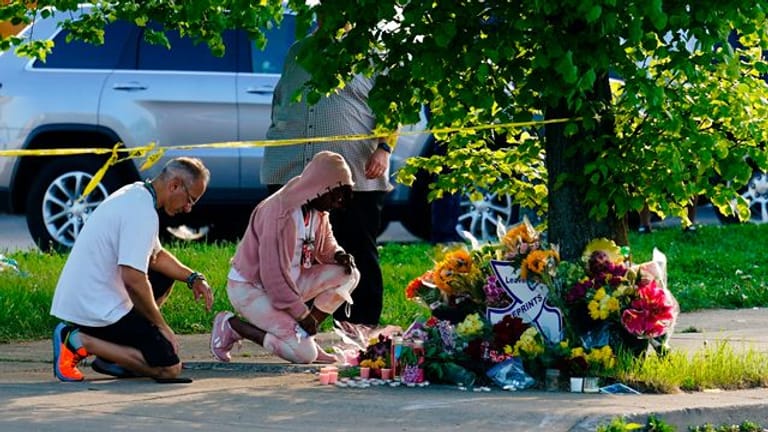Menschen knien vor Blumen, um den Opfern tödlicher Schüsse in einem Supermarkt in Buffalo die letzte Ehre zu erweisen.