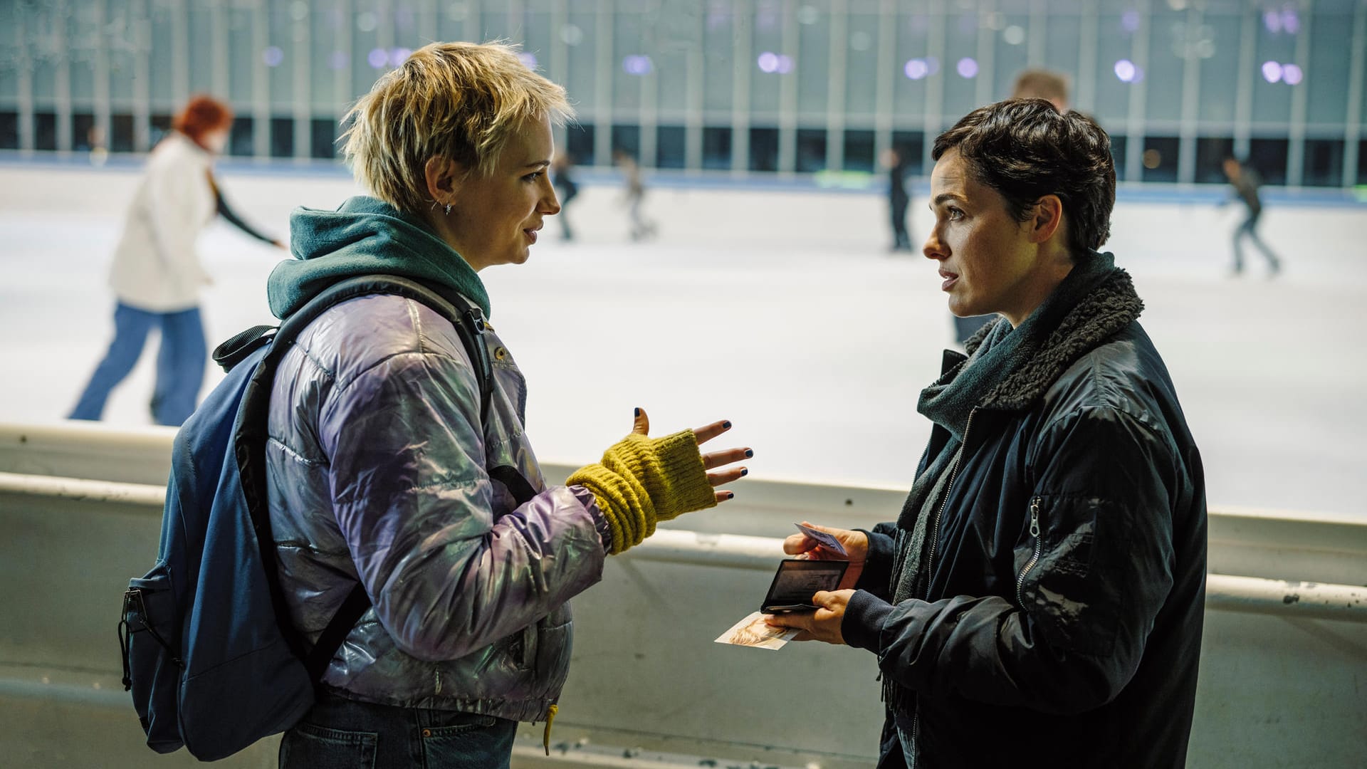 "Polizeiruf 110: Das Licht, das die Toten sehen": Bessie Eyckhoff (Verena Altenberger) befragt in der Eishalle Stefanie Reither (Zoë Valks) und zeigt ihr das Foto von Laura.