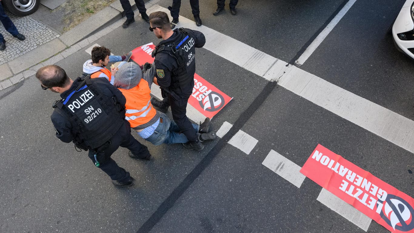 Dresden: Umweltaktivisten der Gruppe "Letzte Generation" haben sich auf der Fahrbahn festgeklebt und werden von Polizisten abgeführt.