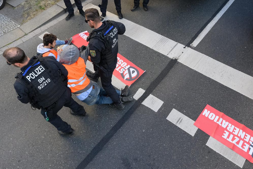 Dresden: Umweltaktivisten der Gruppe "Letzte Generation" haben sich auf der Fahrbahn festgeklebt und werden von Polizisten abgeführt.