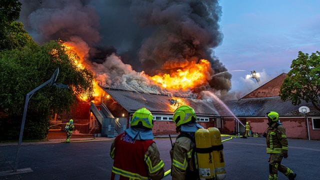 Eine brennende Sporthalle wird von Feuerwehrleuten gelöscht (Archivbild): Wie es zu dem Brand kam, ist noch nicht geklärt.