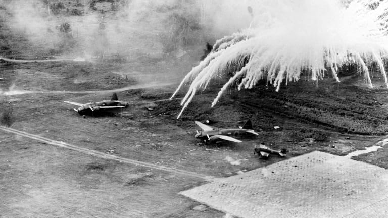 Weiße Phosphorbomben explodieren über einem japanischen Bomber und einem Kampfflugzeug auf dem ehemaligen Flugplatz Lakunai: Die Waffe zählt zu den Brandbomben.