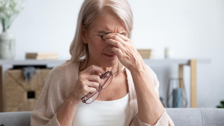 Ältere Frau reibt ihre Augen: Gerötete, brennende Augen sind ein typisches Zeichen dafür, dass dem Auge Feuchtigkeit fehlt. Die Ursachen sind manchmal banal. Es können aber auch ernste Erkrankungen dahinterstecken.
