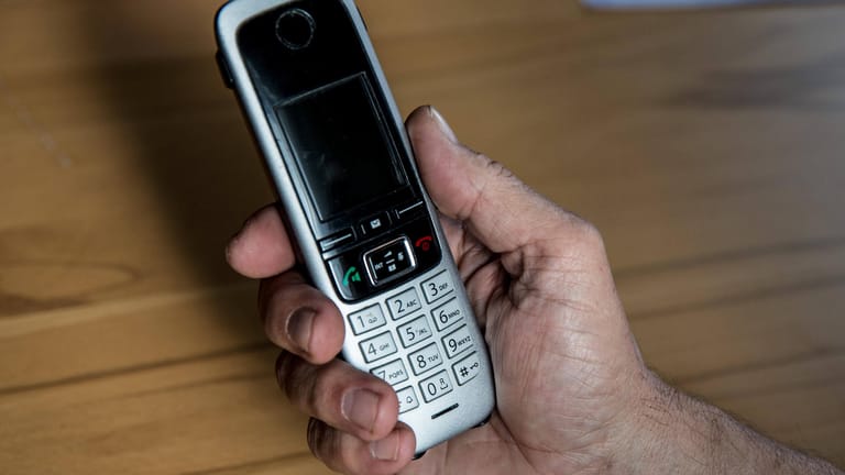 Die Hand eines älteren Menschen hält ein Telefon (Symbolbild): Falsche Polizisten haben in Bayern 2021 über 6 Millionen Euro gestohlen.