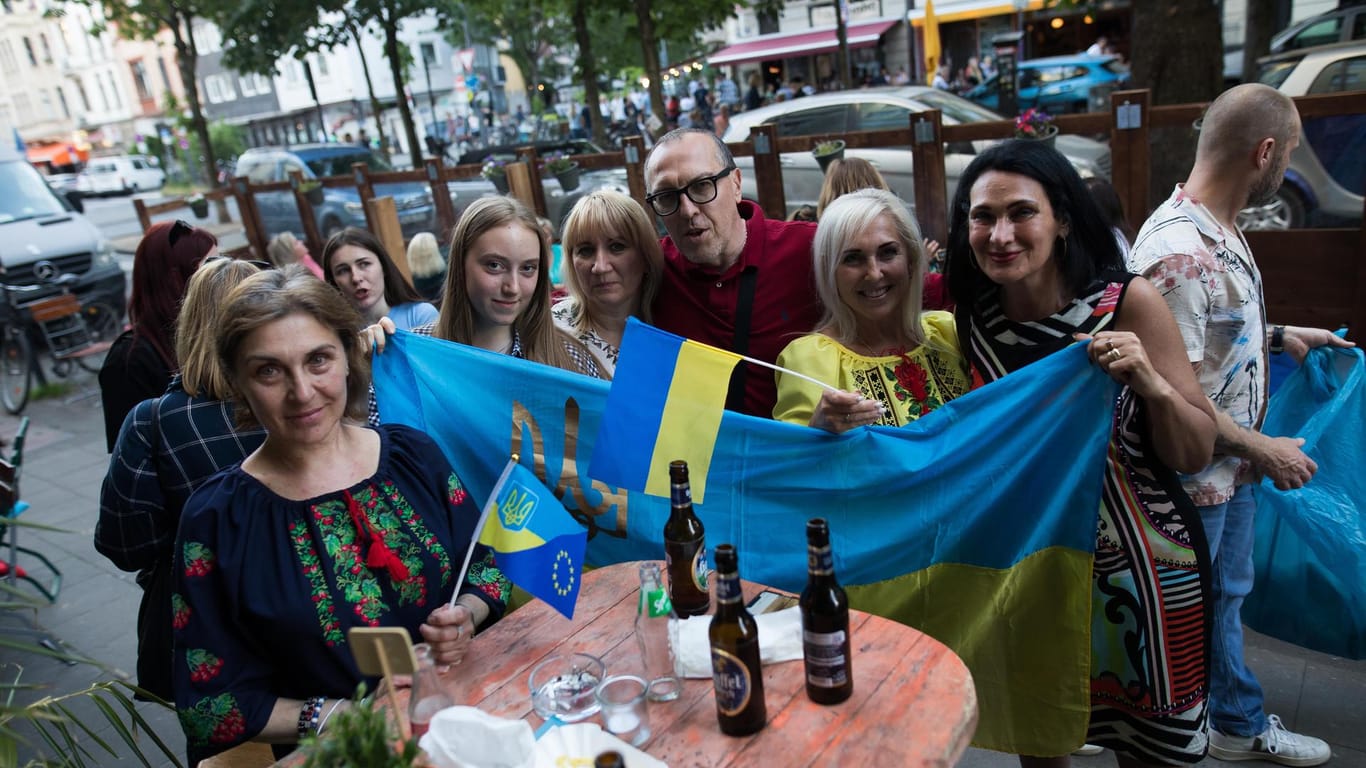 Besucher des Café Selenskyj halten eine ukrainische Flagge: Das Café in der Bagatelle Bar öffnet jeden Sonntag für ukrainische Geflüchtete seine Türen.