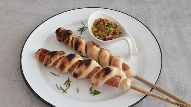 Das Stockbrot wird schlangenmäßig um den Hotdog gewickelt und gegrillt.